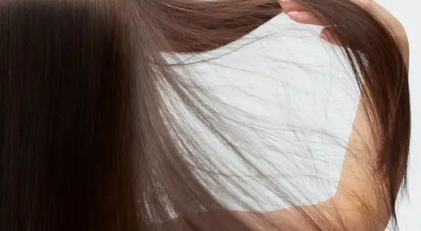 Mano acariciando su pelo fino y ondulado, de color castaño oscuro, que cae en cascada.