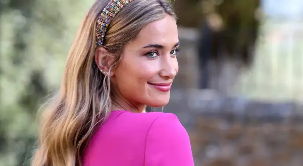 Joven sonriente con un peinado juvenil para boda, luciendo una diadema de pedrería y un vestido fucsia.