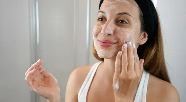 Mujer con espuma en el rostro, aplicándose un limpiador facial con ácido glicólico y niacinamida.