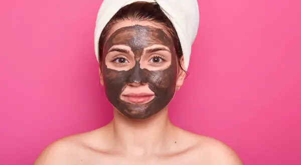 Una mujer con una toalla en la cabeza y una mascarilla de barro en la cara cansada, lista para un tratamiento de spa.