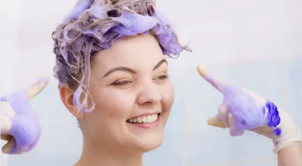 Sonrisa radiante con cabello teñido de violeta, lista para el antes y después. Guantes con espuma violeta.