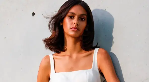 Mujer con cabello castaño brillante y piel bronceada, luciendo un vestido blanco. Su cabello parece suave, como si hubiera aprendido como se usa el acondicionador.