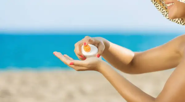 Mujer con sombrero aplicando crema solar en la mano. ¡No dejes que la crema solar caduca te arruine el día en la playa!