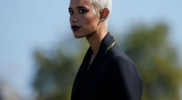 Mujer con pelo blanco corto y maquillaje dramático, luciendo un pendiente llamativo en la oreja.