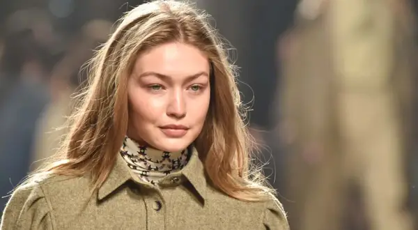 Modelo con cabello rubio y mechas blancas, viste una chaqueta verde y un pañuelo estampado.