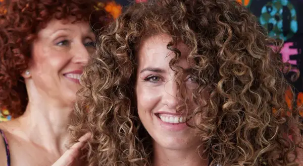 Dos mujeres sonríen, una con cabello rizado pelirrojo y la otra con cabello rizado castaño, mostrando estilos de cortes de pelo afro.