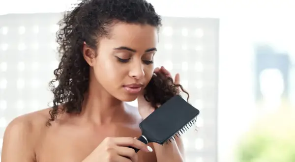 Mujer con pelo rizado y enredado, intentando desenredar con un cepillo negro.