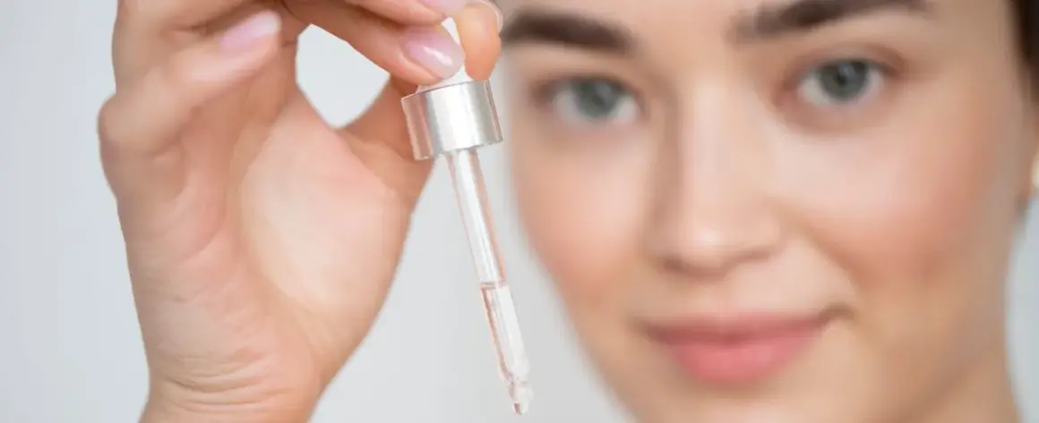 Mujer sosteniendo un gotero con líquido transparente cerca de su rostro.