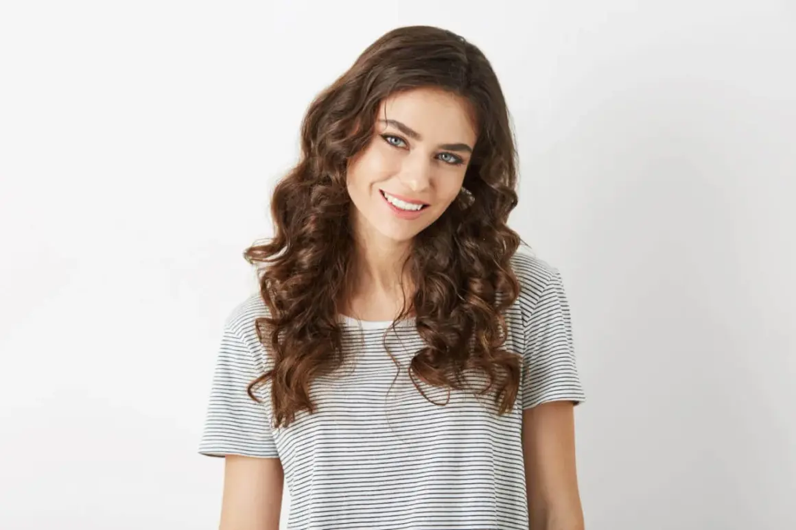 Mujer sonriente con pelo ondulado castaño, ojos azules y camiseta a rayas.