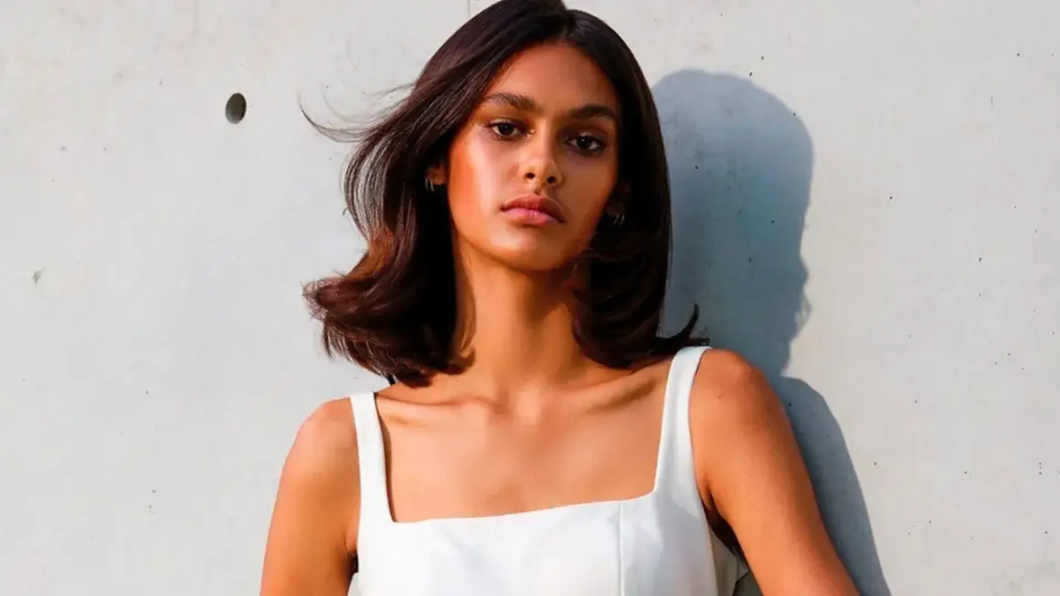 Mujer con cabello castaño brillante y piel bronceada, luciendo un vestido blanco. Su cabello parece suave, como si hubiera aprendido como se usa el acondicionador.