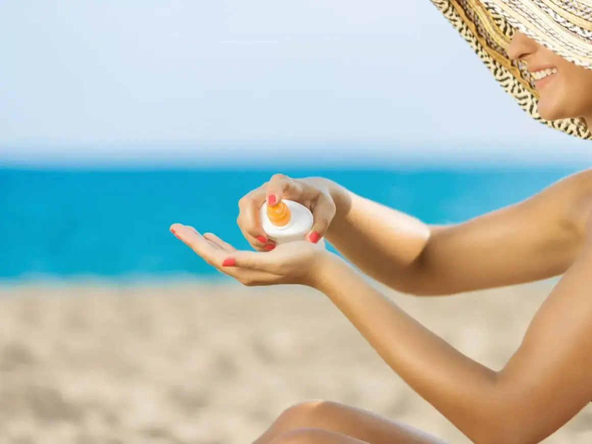Mujer con sombrero aplicando crema solar en la mano. ¡No dejes que la crema solar caduca te arruine el día en la playa!