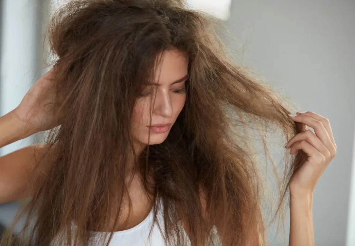 Mujer con pelo deshidratado, sin brillo y enredado, tocándose la cabeza con preocupación.