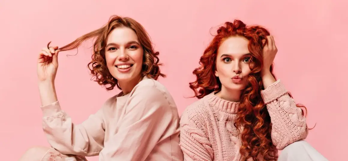 Dos chicas con diferentes tipos de cabello ondulado, una sonríe y juega con su pelo, la otra hace un puchero.
