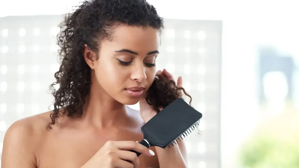 Mujer con pelo rizado y enredado, intentando desenredar con un cepillo negro.