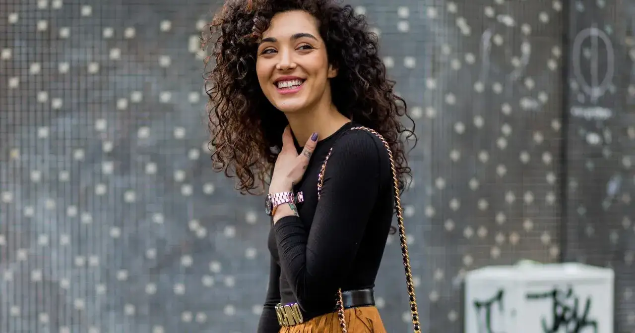 Mujer con pelo rizado y oscuro, sonriendo. Su cabello luce como si hubiera aprendido como rizar el pelo con estilo.