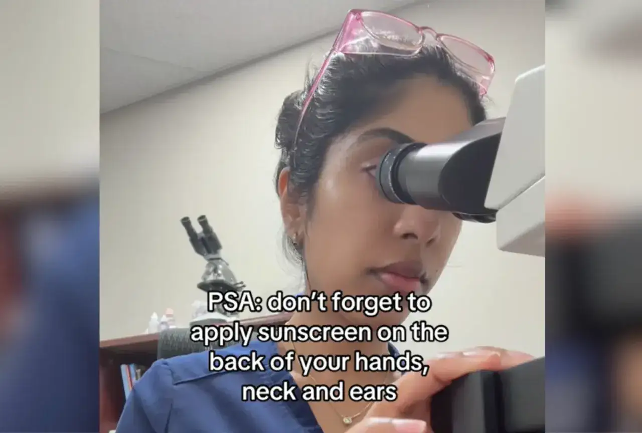 Mujer con gafas rosas mira por un microscopio. Recordatorio: el spf protege tu piel.