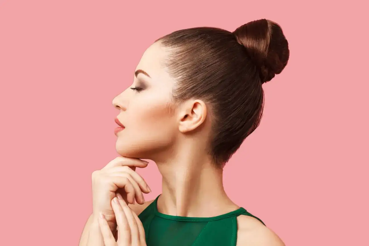 Perfil de mujer con un elegante mo&ntilde;o alto, ojos cerrados y mano en la barbilla.
