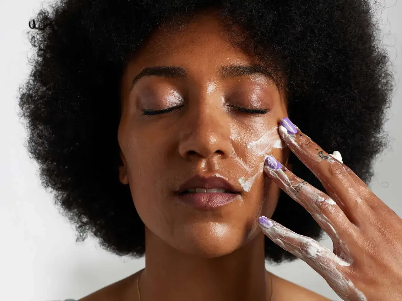 Mujer con piel oscura aplicándose crema en la cara. Una rutina para cerrar poros de la cara.