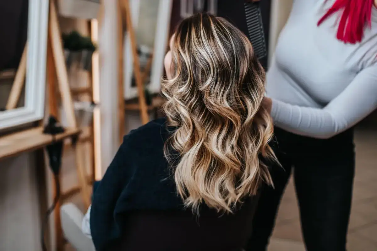 Cabello con balayage rubio, ondas suaves y un toque de color vibrante en la parte superior.