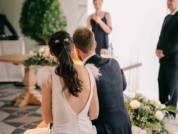 Novia con coleta baja adornada con horquillas, ideal para peinados para boda civil. El novio, de traje oscuro, la acompaña.