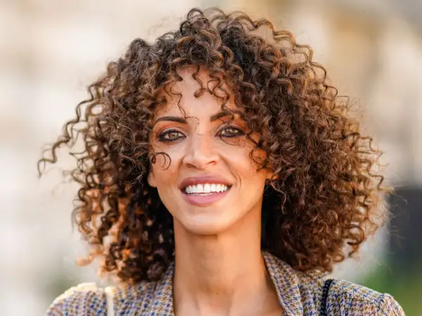 Mujer con rizos voluminosos y un estilo que evoca los peinados años 20. Su pelo rizado luce natural y lleno de vida.