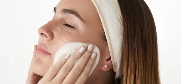 Mujer con diadema aplicándose espuma limpiadora en el rostro, parte de su rutina facial de noche.