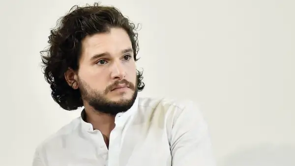 Hombre con pelo rizado oscuro y barba, viste camisa blanca.