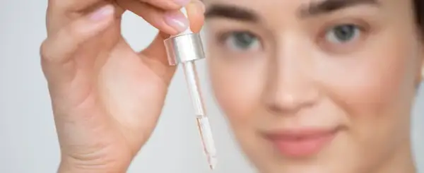 Mujer sosteniendo un gotero con líquido transparente cerca de su rostro.