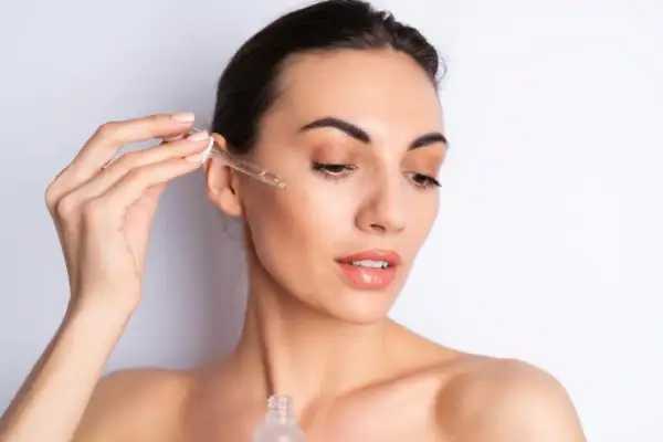 Una mujer aplica serum en su rostro con un gotero. Así se aplica el serum para una piel radiante.