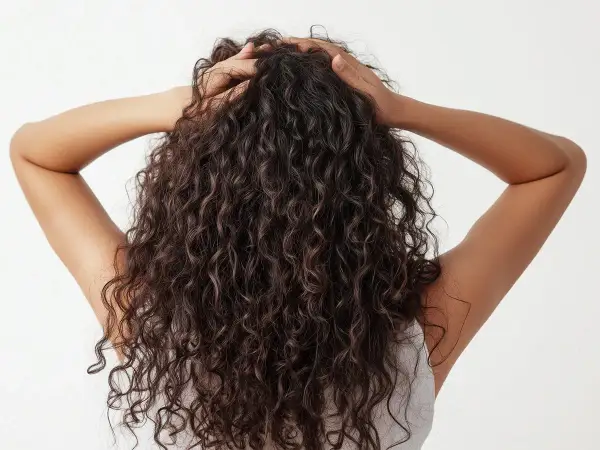 Mujer con pelo crespo oscuro y voluminoso, con las manos en la cabeza, mostrando la textura natural de su cabello.