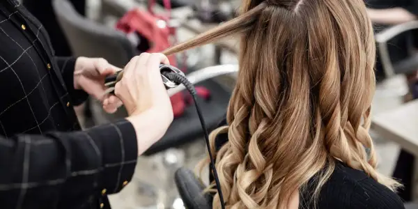 Manos expertas usando una tenaza para rizar el cabello rubio y castaño, creando ondas perfectas.