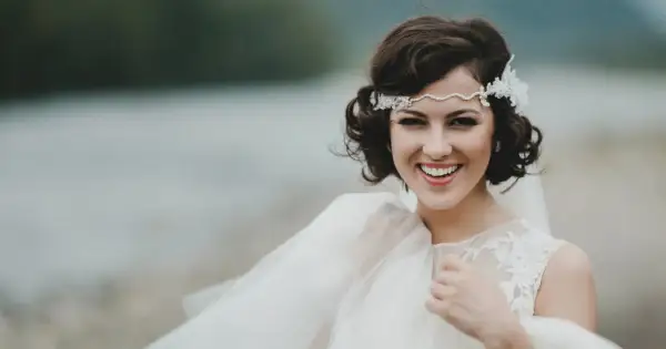 Novia sonriente con semirecogido pelo corto boda, diadema de perlas y encaje, velo vaporoso.
