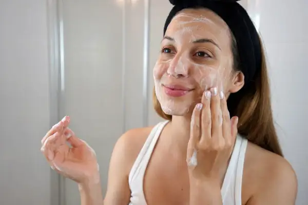 Mujer con espuma en la cara, disfrutando de su rutina de limpieza facial en casa.