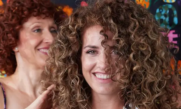 Dos mujeres sonríen, una con cabello rizado pelirrojo y la otra con cabello rizado castaño, mostrando estilos de cortes de pelo afro.